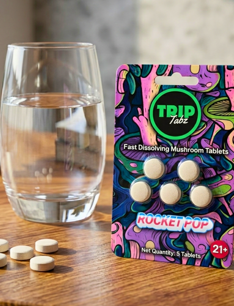 TRIP Labz Rocket Pop fast-dissolving mushroom tablets packaging with tablets and a glass of water on a wooden surface.