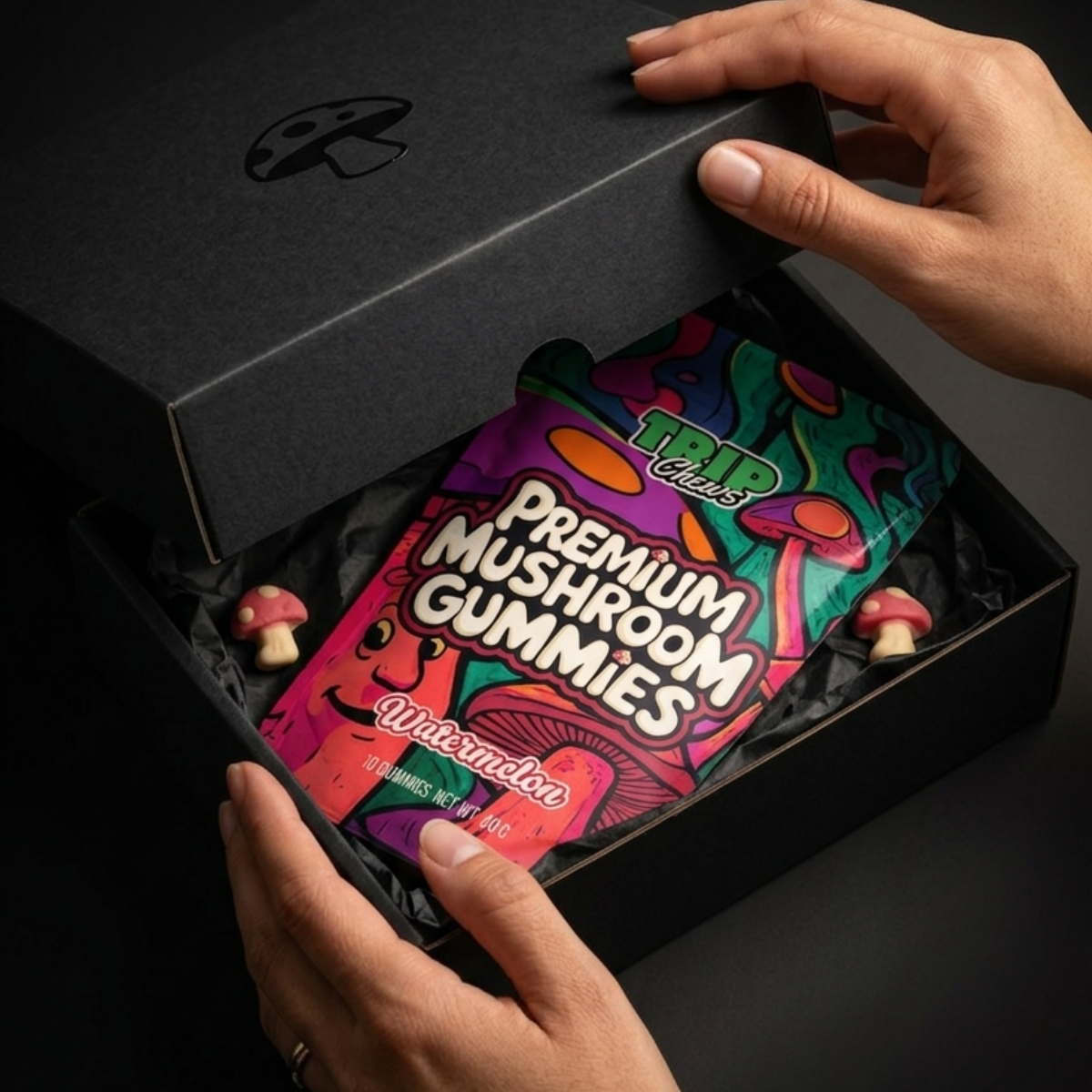Person opening a black box to reveal a package of 'Premium Mushroom Gummies' with colorful packaging.