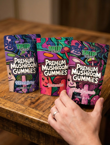 Three packages of Trip Chews Premium Mushroom Gummies on a wooden surface with a hand reaching for one.